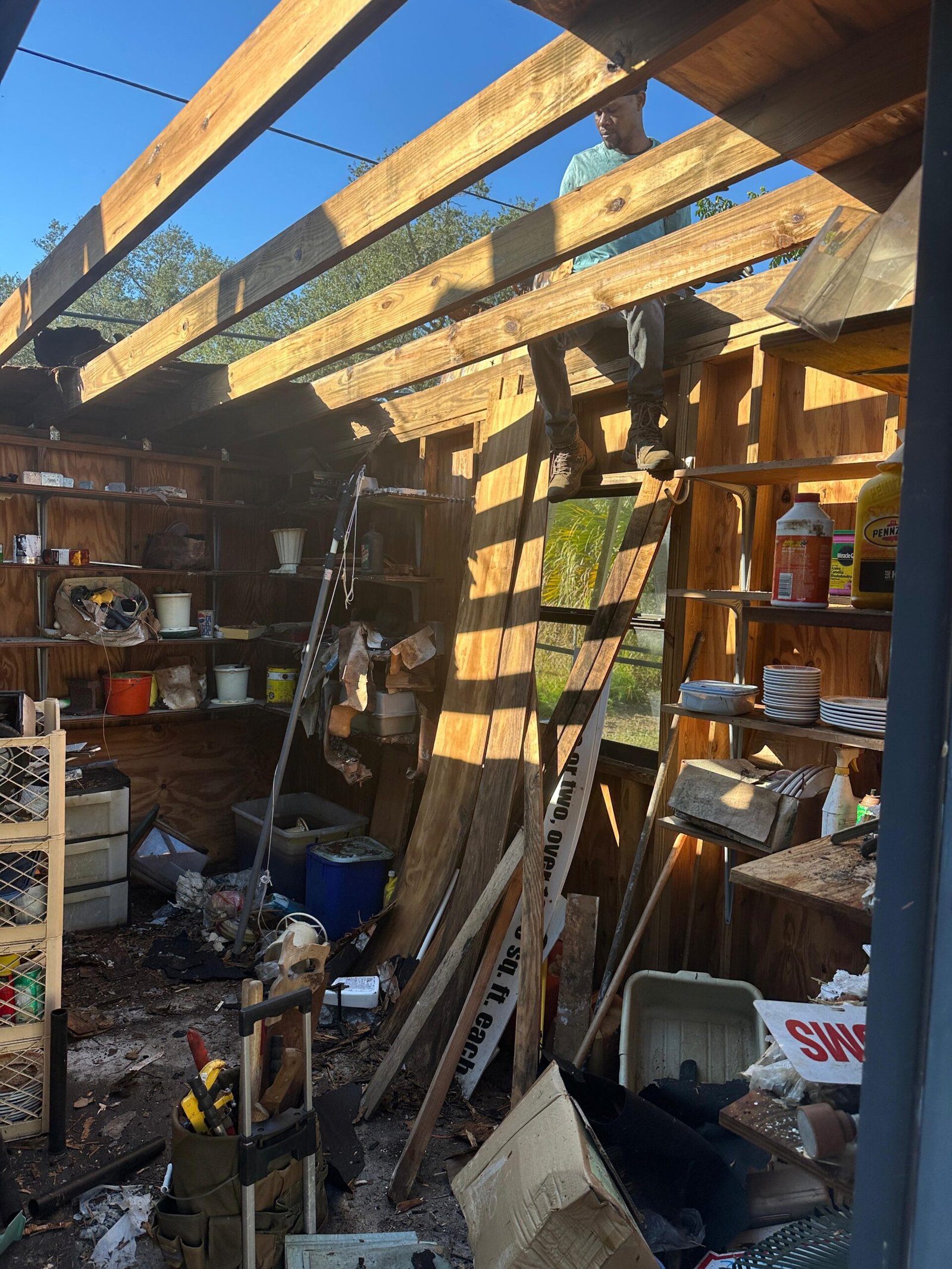 Shed teardown in progress with exposed framing and active debris removal.