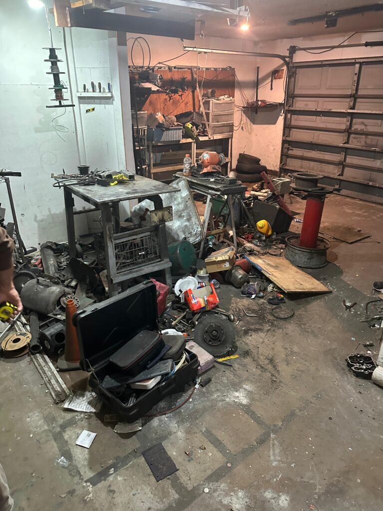 Cluttered garage full of tools, scrap metal, and workbenches before cleanout