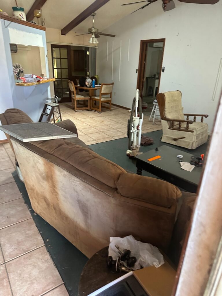 Living room crowded with furniture, boxes, and household items before cleanout
