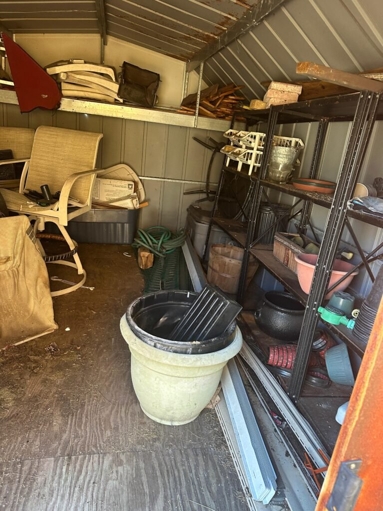 Storage shed packed with patio furniture, bins, and shelving before cleanout