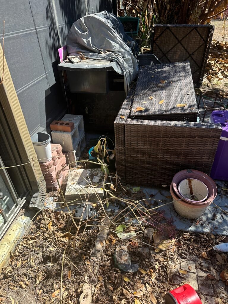Outdoor storage nook with covered furniture and stacked pots before cleanout
