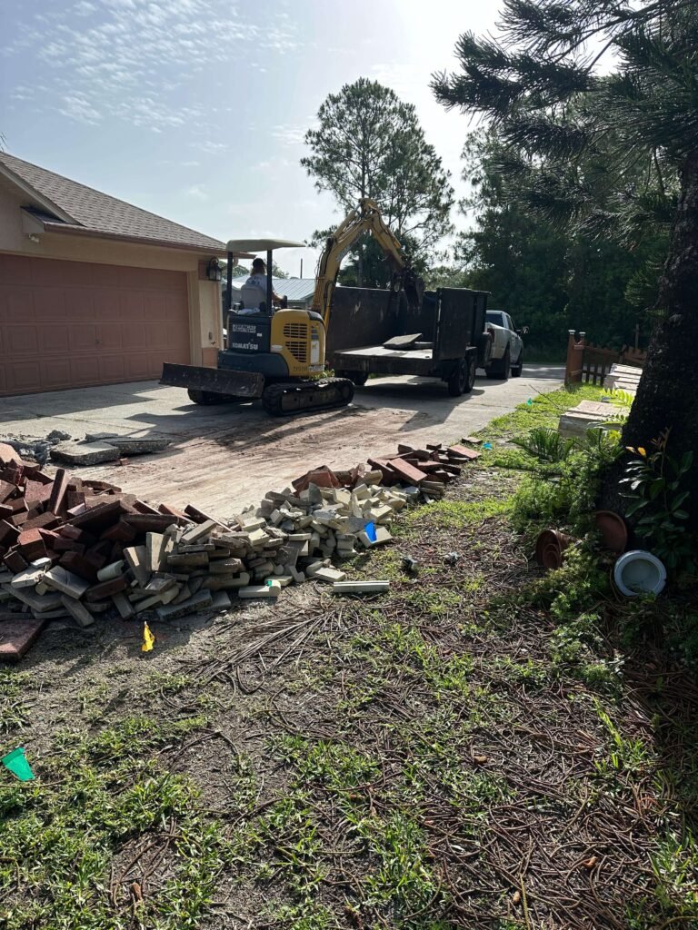 Concrete driveway slabs being removed by excavator into trailer Palm Bay — concrete demolition and hauling