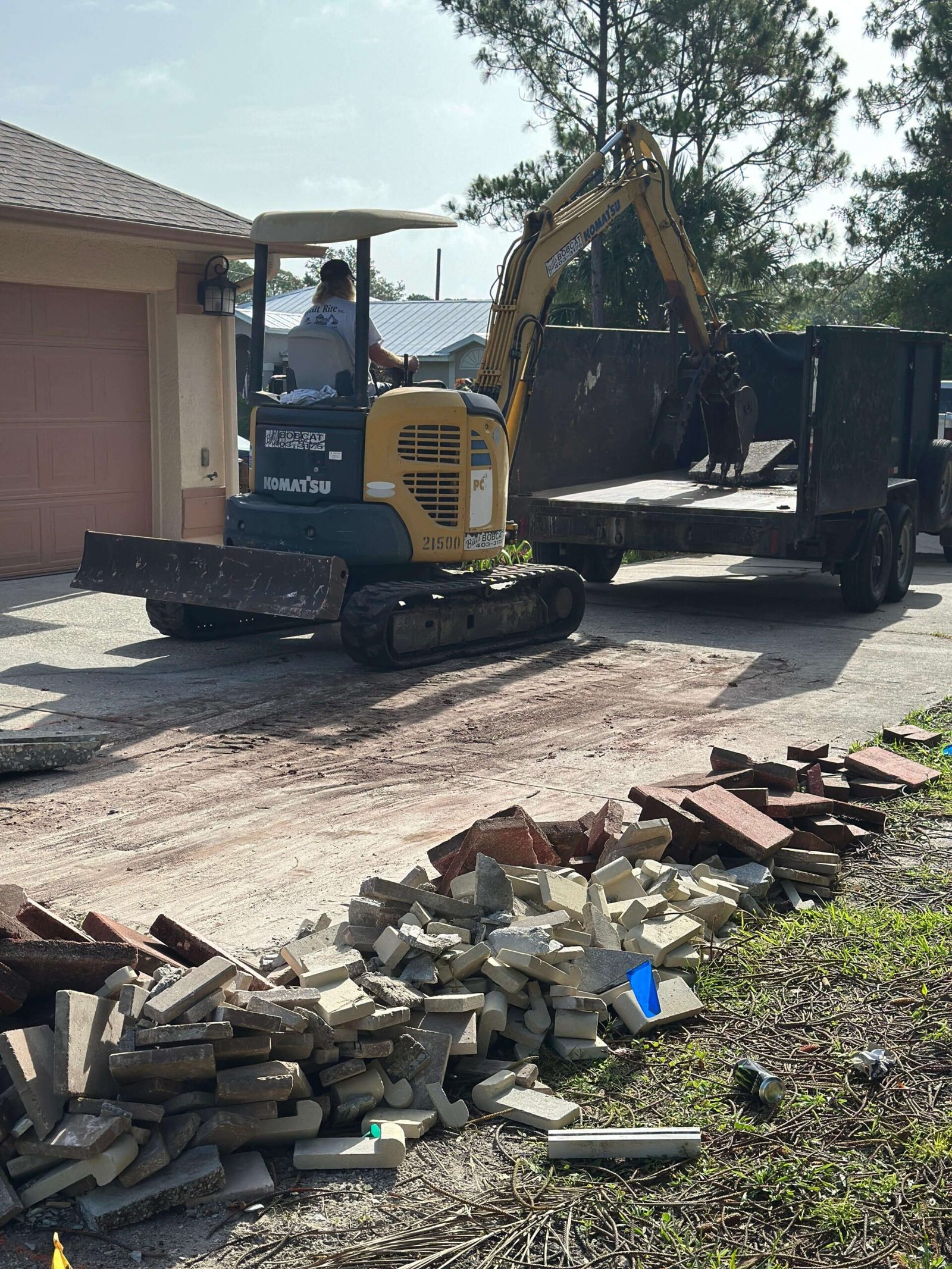 Komatsu excavator loading concrete debris onto trailer during driveway removal Palm Bay FL
