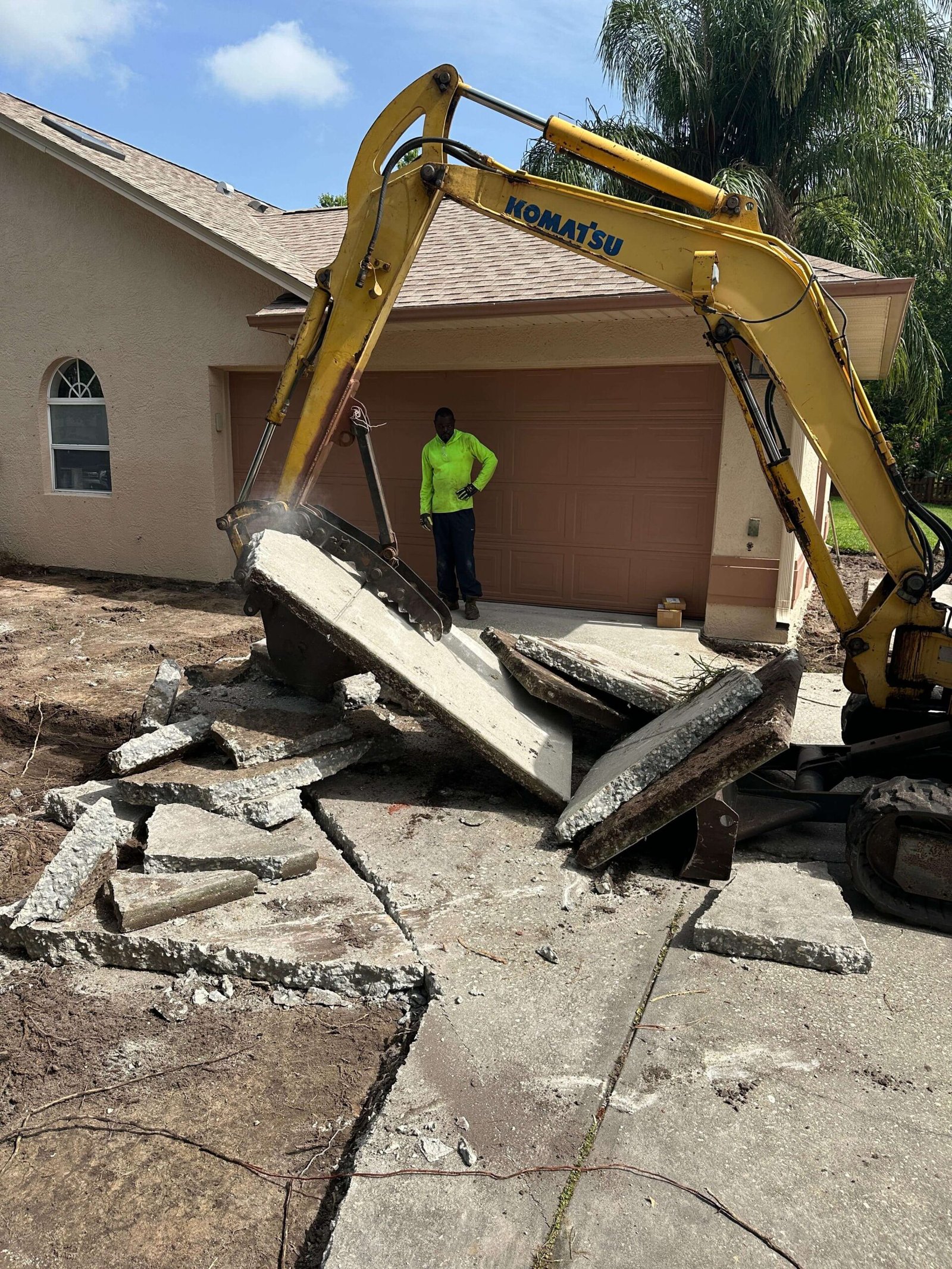 Excavator breaking up a concrete driveway during a demolition project in Palm Bay, FL